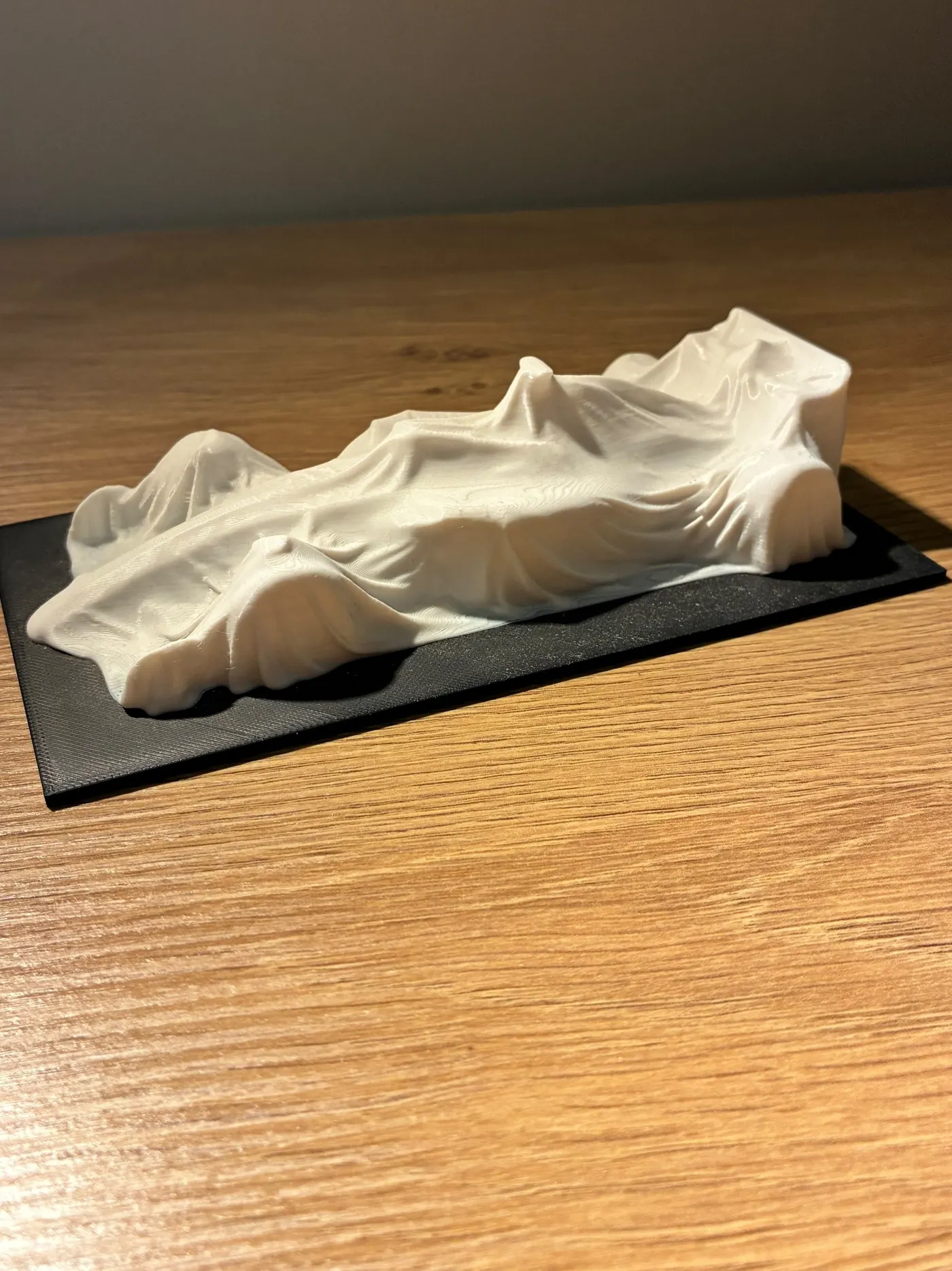 White 3D printed sculpture of a race car under a draped cover on a black base