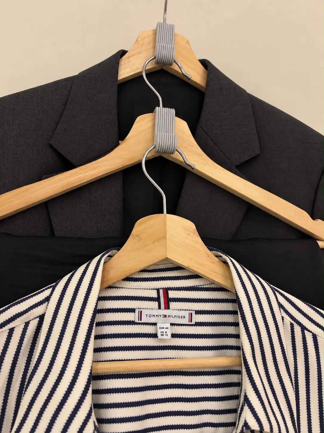 Grey 3D printed connector hooks linking three wooden hangers vertically, holding a blazer and a striped shirt