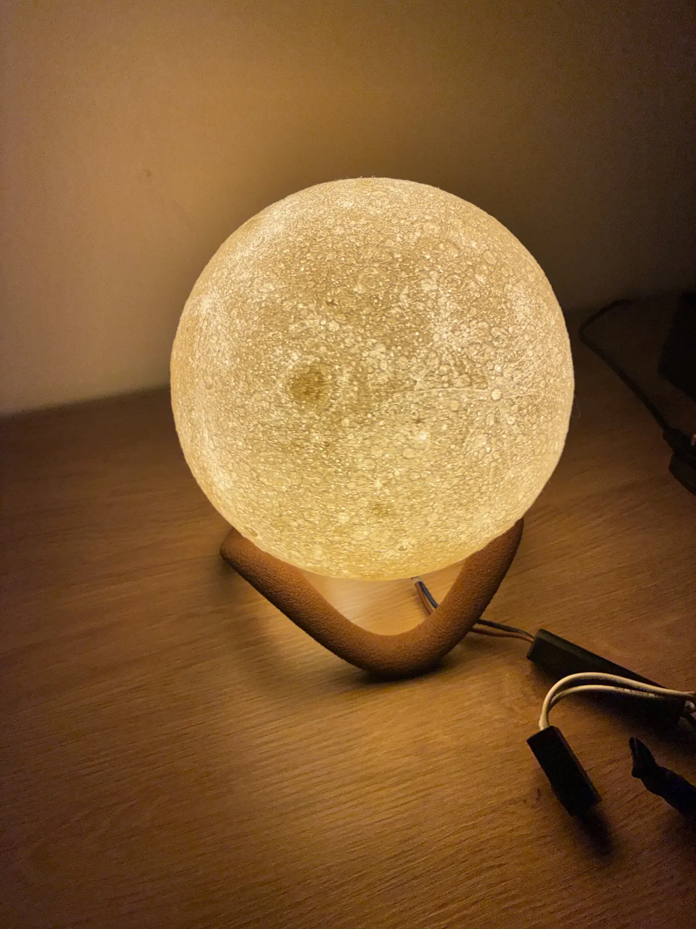 Glowing 3D printed moon lamp with detailed crater surface on a curved stand