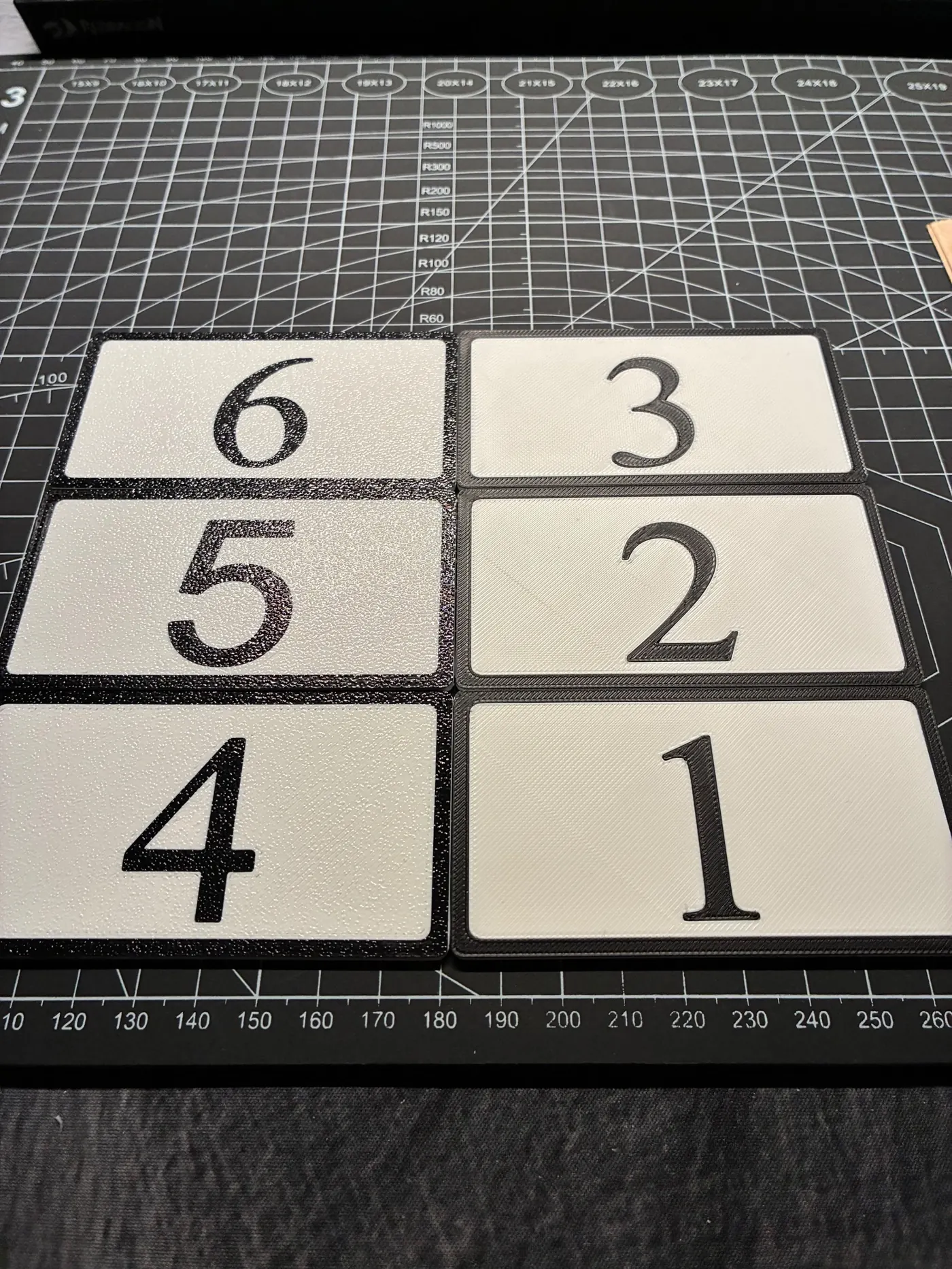 Six white rectangular plates with black raised numbers 1 to 6 and black borders on a cutting mat