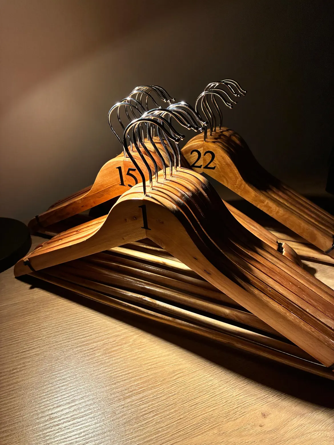 Stacks of natural wooden hangers with black serif numbers 1, 15 and 22, lit by warm side light
