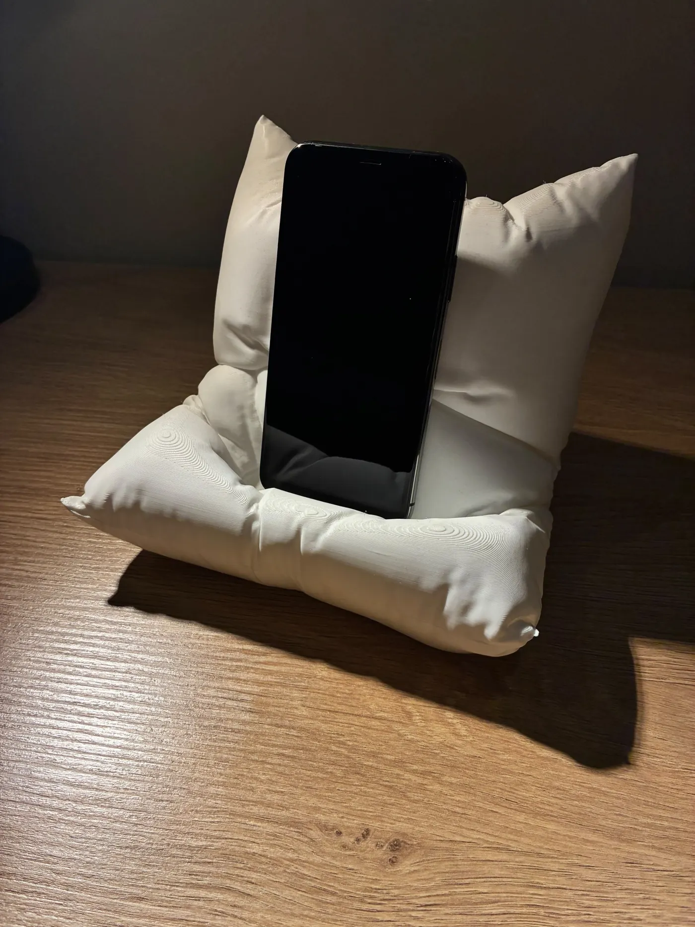 White 3D printed phone stand shaped like a folded pillow holding a smartphone