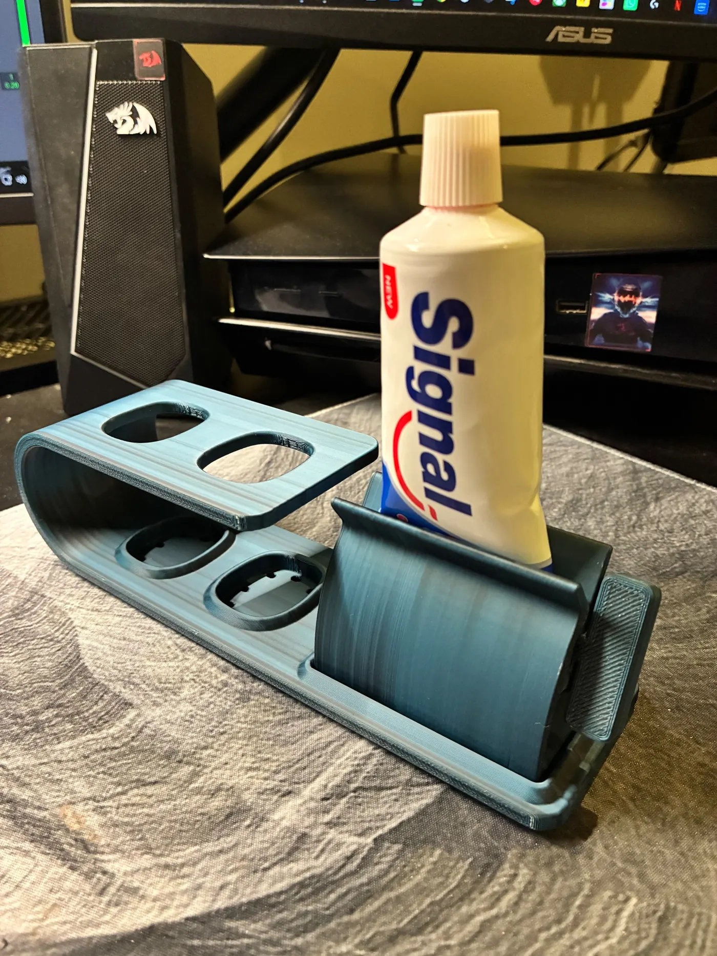 Slate blue 3D printed bathroom organizer with two toothbrush holes and a toothpaste tube in a roller slot